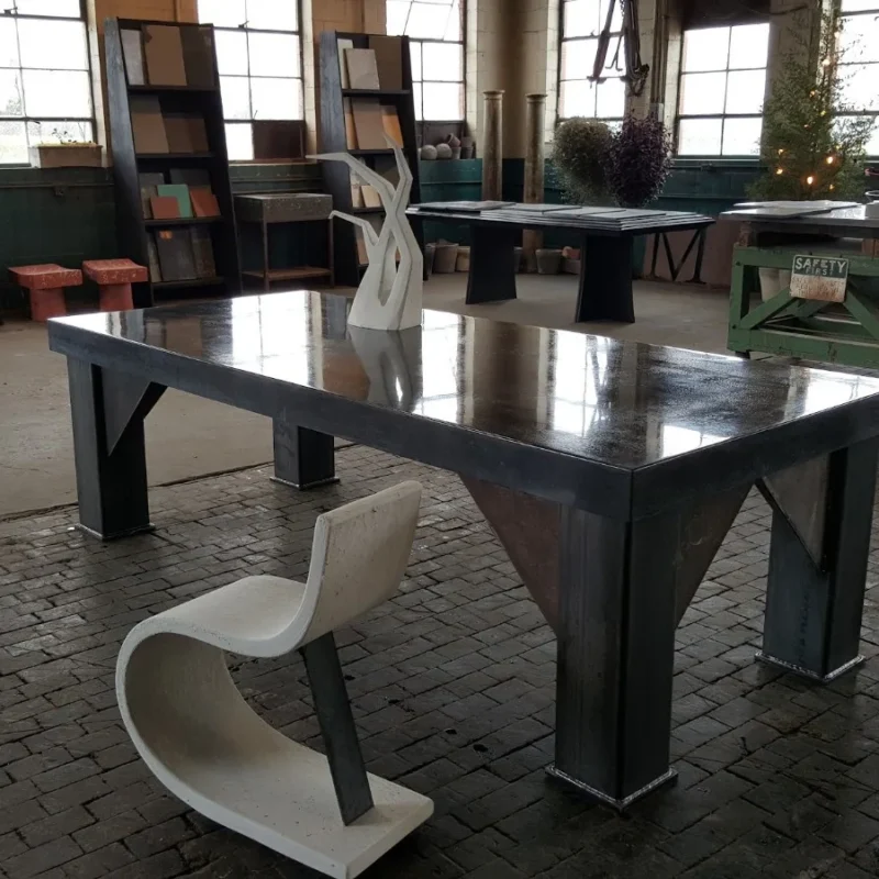 Modern furniture showroom with sleek black dining table, white sculptural chairs, shelving units, and industrial windows in contemporary warehouse space