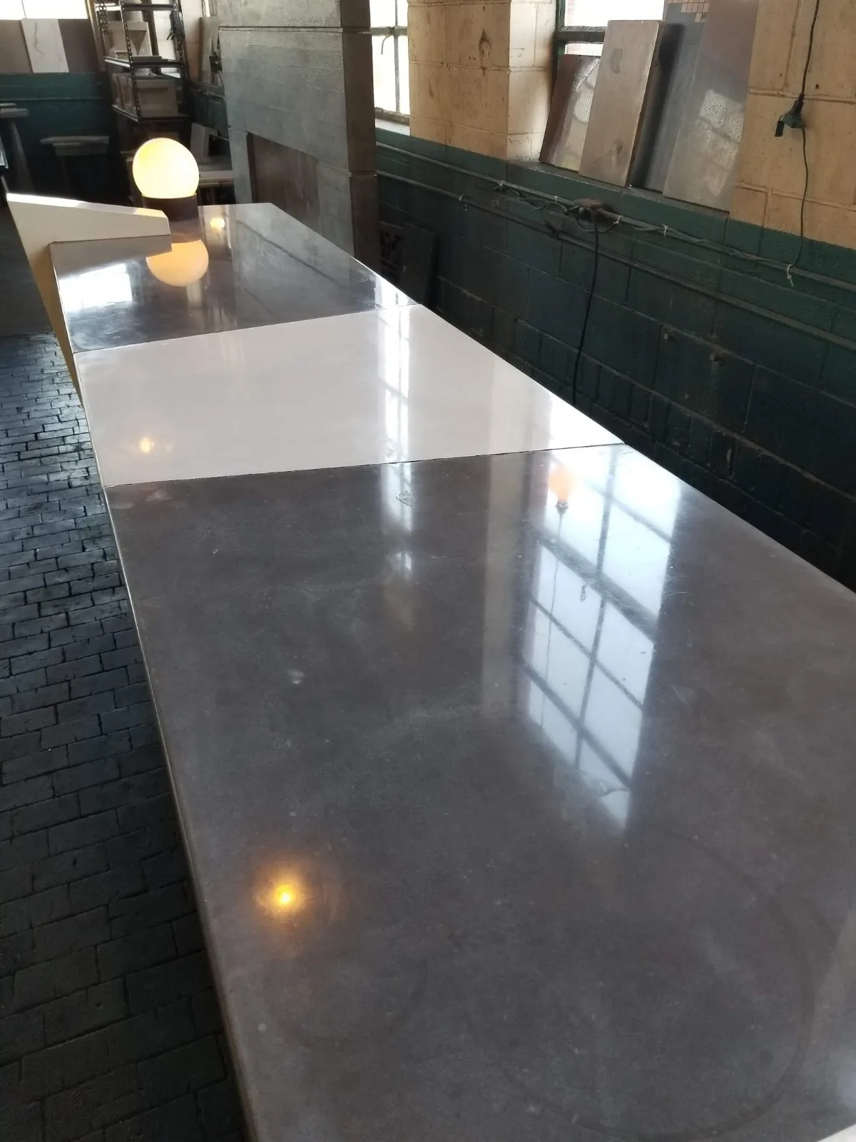 Long polished concrete counter or table in industrial workshop with white section and dark gray section, reflecting natural light from windows and overhead fixtures