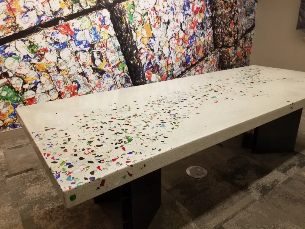 A long white terrazzo bench with colorful aggregate chips sits in front of a vibrant abstract mural featuring a dark tree branch and multicolored paint splatters
