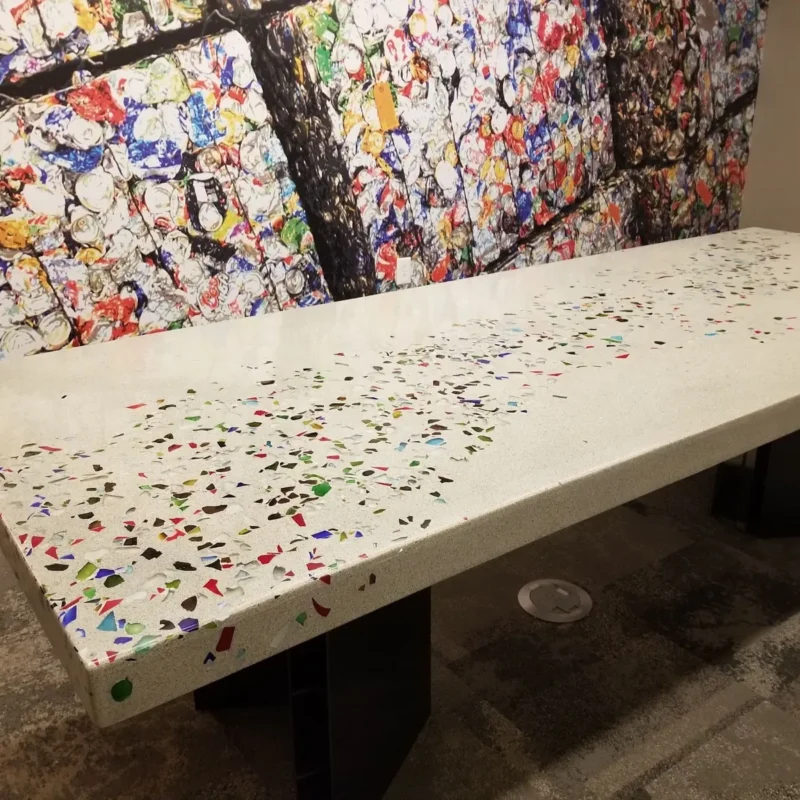 A long white terrazzo bench with colorful aggregate chips sits in front of a vibrant abstract mural featuring a dark tree branch and multicolored paint splatters