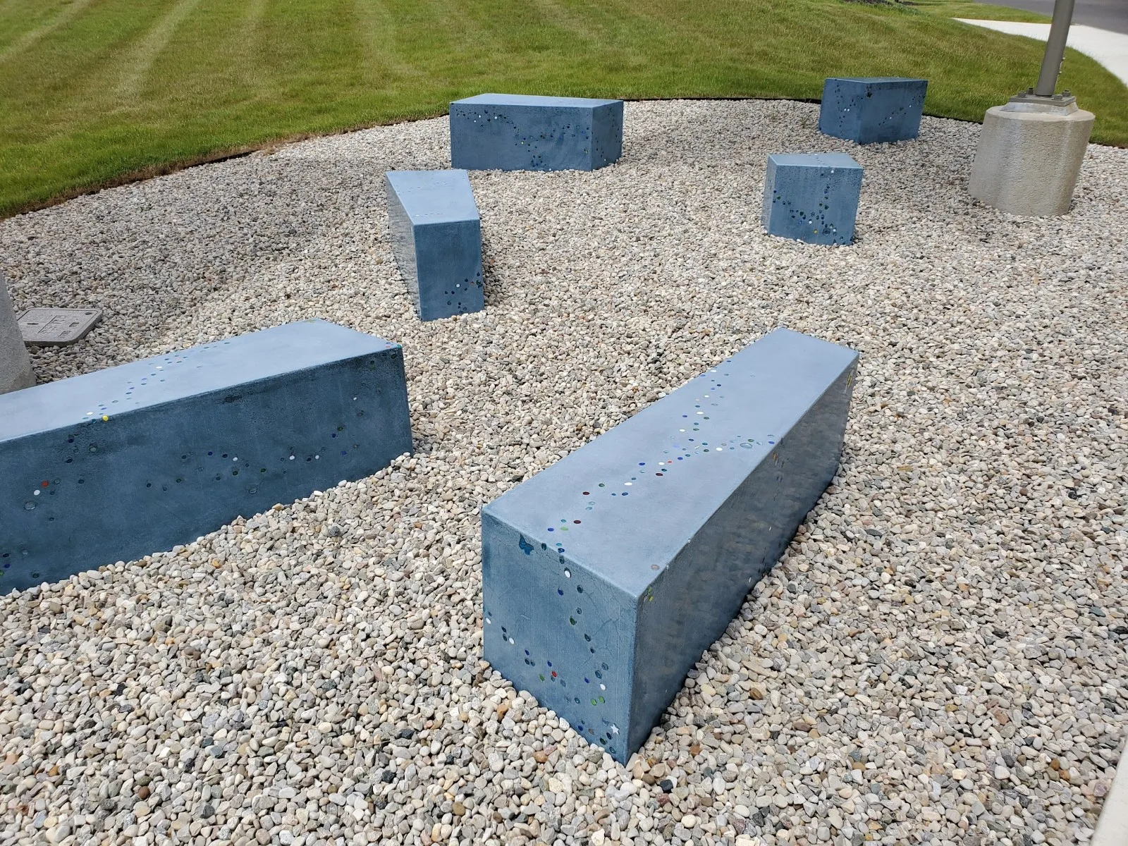 Concrete benches and bollards arranged on gravel in an outdoor plaza near manicured lawn
