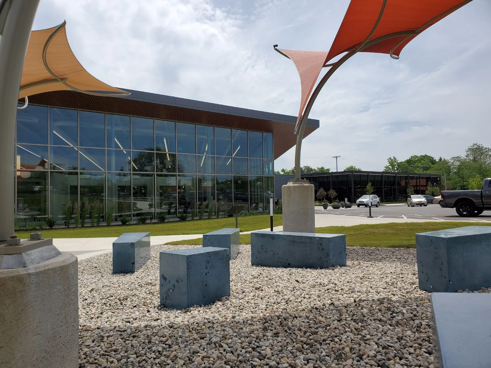 Modern commercial building with floor-to-ceiling windows and colorful shade sails in Cincinnati, featuring concrete seating blocks and gravel courtyard