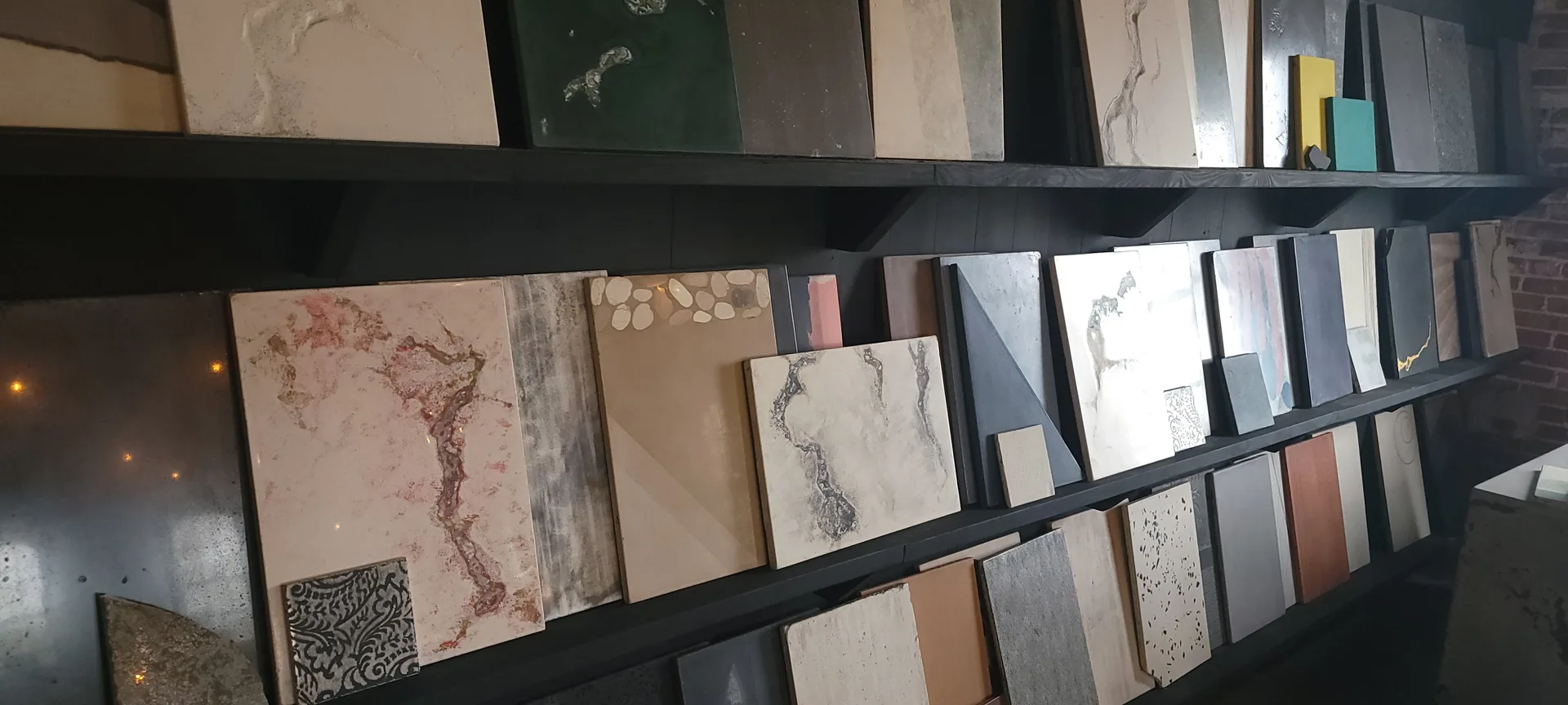 Black shelving display with tile and stone samples including marble, granite, and textured finishes in neutral tones and earth colors