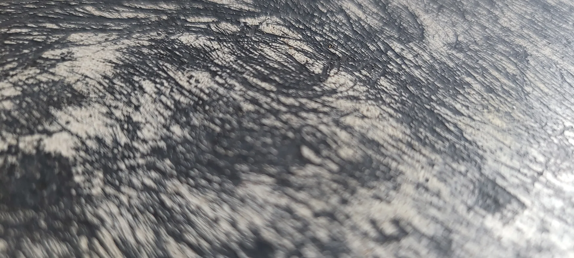 Close-up of rough, textured gray and white surface with diagonal striations and weathered patterns, resembling concrete or stone with sharp shadows cast across it
