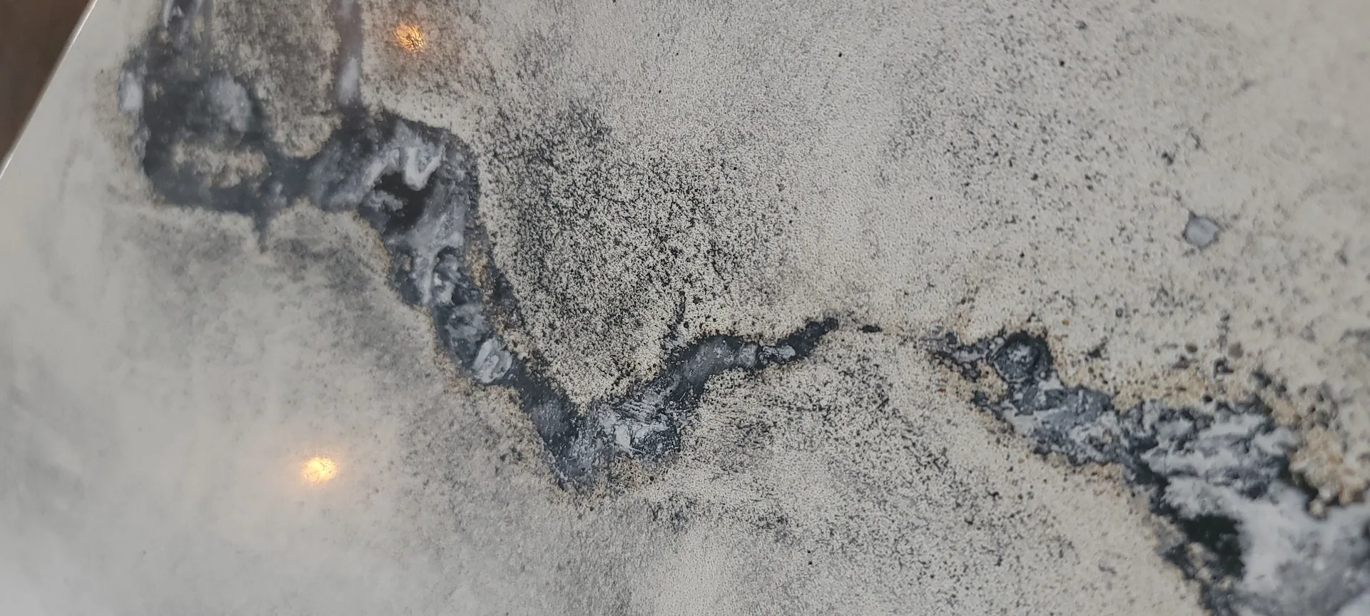 Close-up of concrete floor with dark stains, water damage, and deteriorating patches showing wear and discoloration