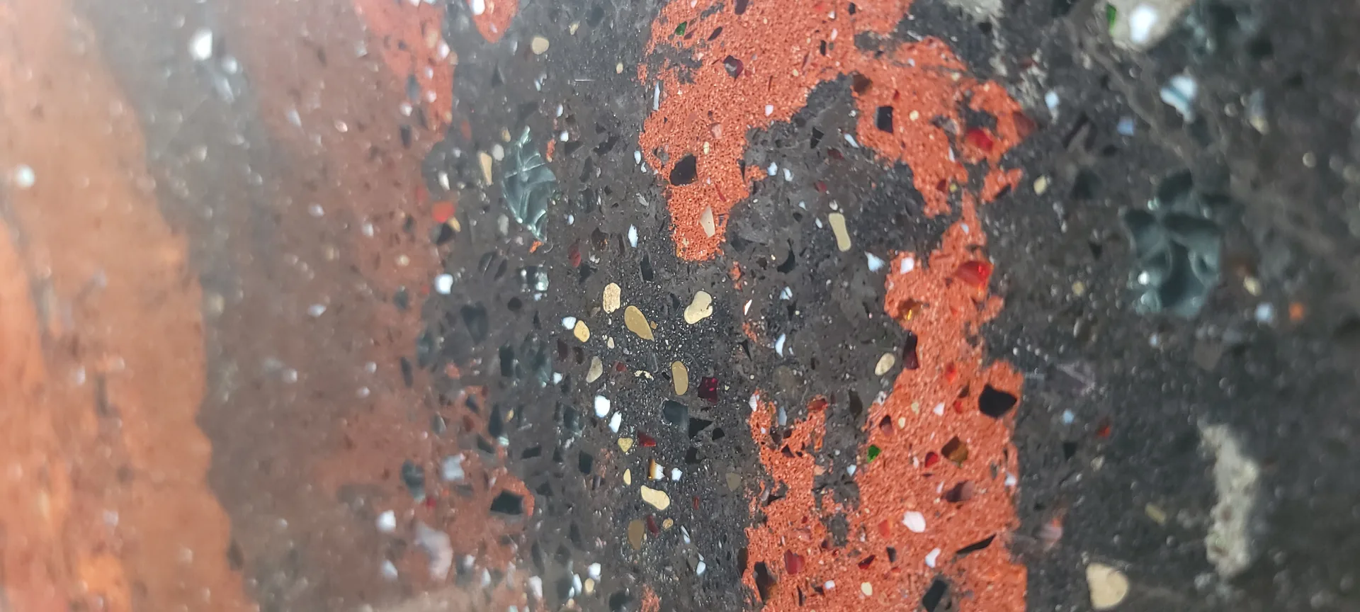Close-up of weathered red and dark brick wall with visible mortar joints, small pebbles, and white speckles embedded in the surface