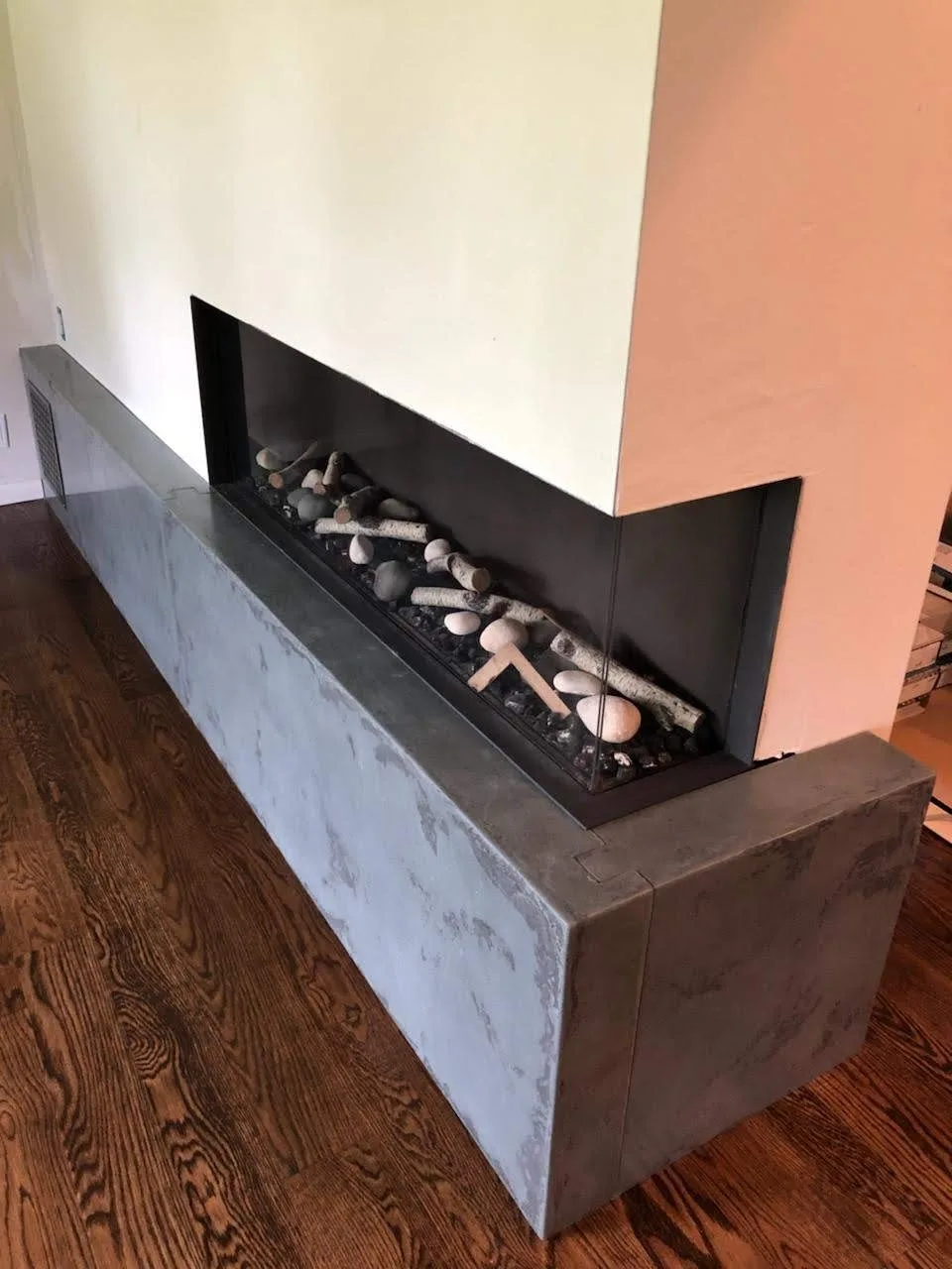 Modern linear fireplace with black metal surround and decorative white and gray logs, mounted on concrete base against white and coral walls