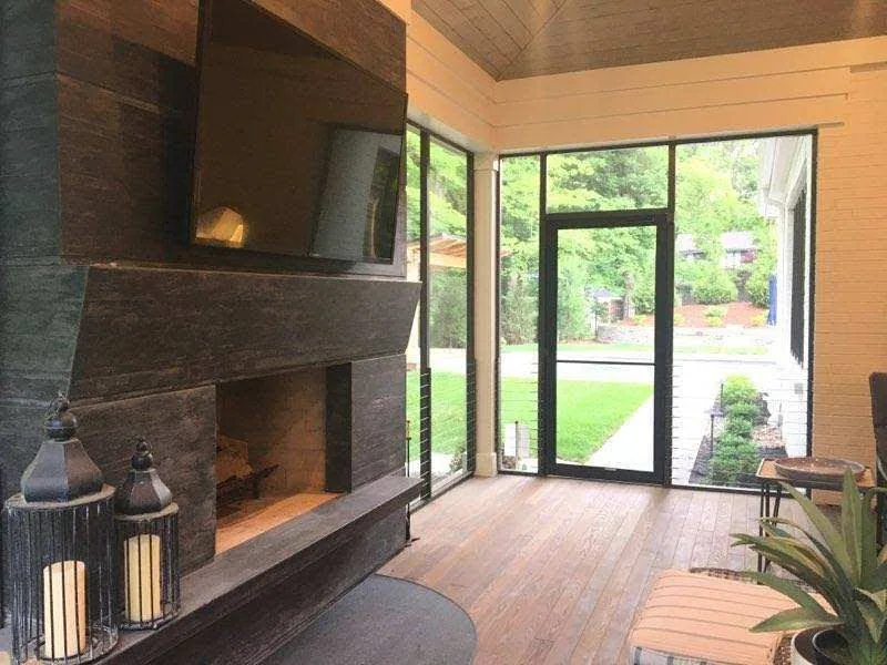 Modern outdoor living space with dark brick fireplace, wooden ceiling, and glass doors opening to landscaped garden with green lawn