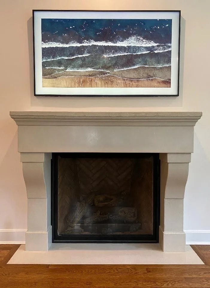 Framed aerial photograph of ocean waves and sandy beach displayed above a cream-colored fireplace mantel in a modern living room