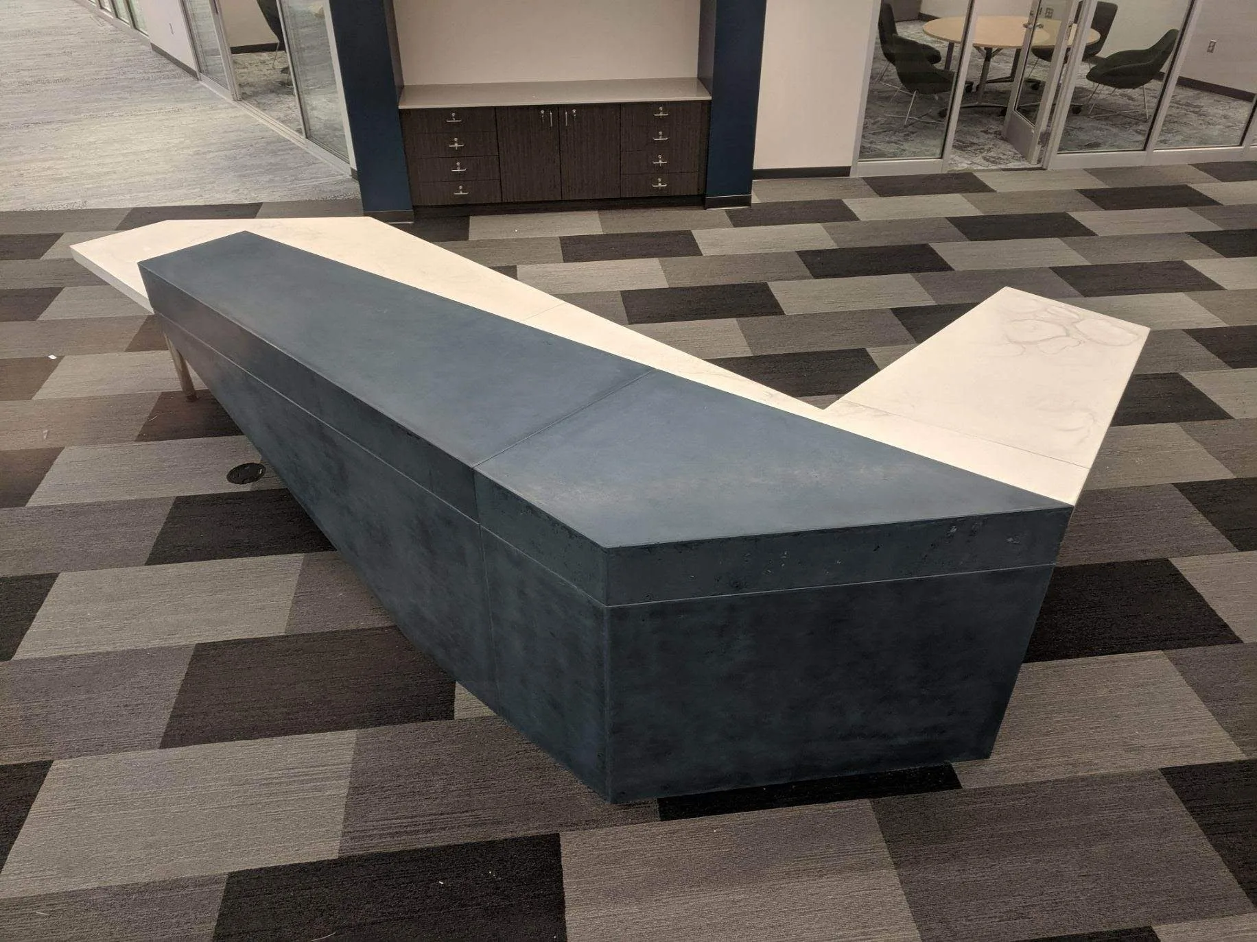 Modern curved reception desk with dark blue-gray base and white curved top in contemporary office lobby with geometric patterned flooring