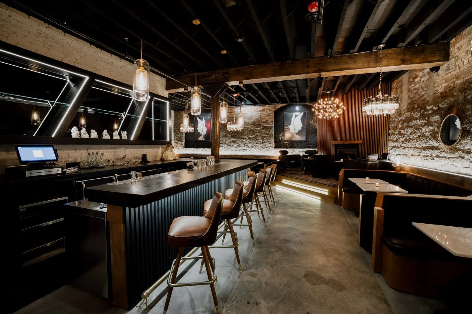 Modern upscale bar interior with exposed brick walls, wooden beams, pendant lighting, and leather bar stools along a black counter in Cincinnati