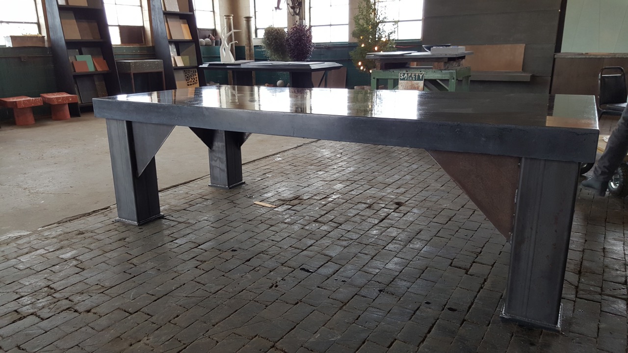 Large modern metal table with polished top in industrial loft space with brick flooring and shelving units