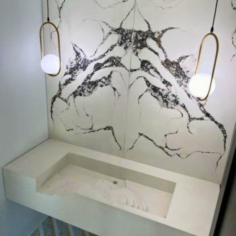 Modern white bathroom sink with black marble veining and two brass pendant lights hanging above