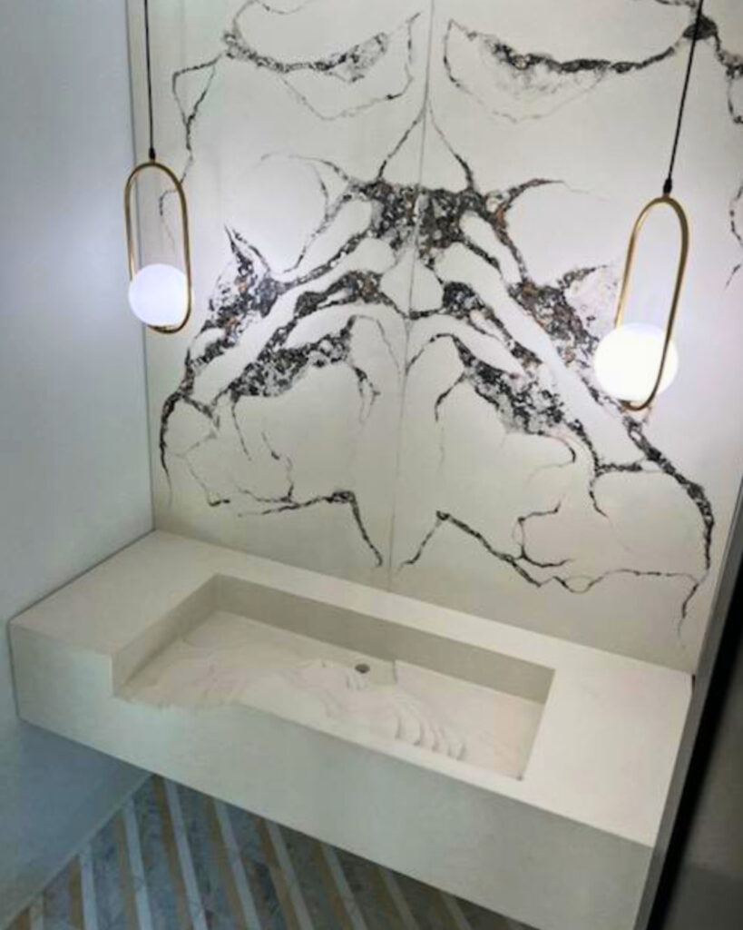 Modern white bathroom sink with black marble veining and two brass pendant lights hanging above