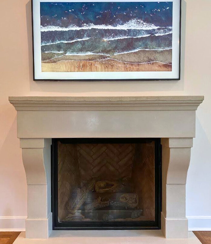 Coastal landscape photograph above cream fireplace mantel showing ocean waves and sandy beach with blue water and white foam
