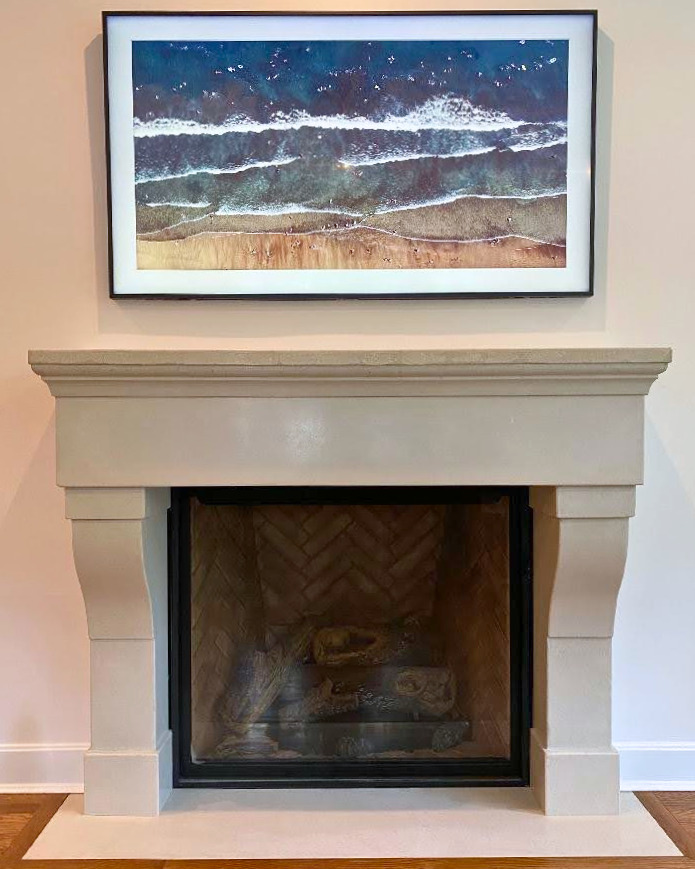 Coastal landscape photograph above cream fireplace mantel showing ocean waves and sandy beach with blue water and white foam