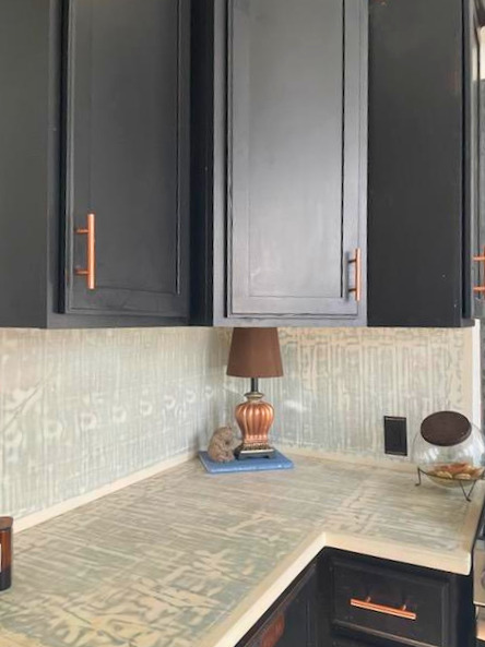 Modern kitchen with dark gray and white cabinetry, tile backsplash, and countertop featuring a decorative lamp and small decor items