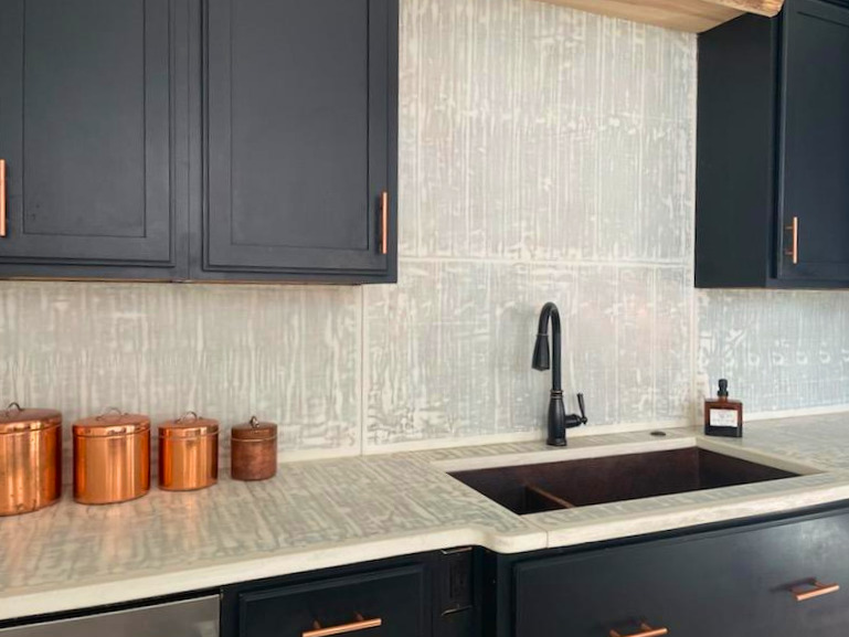 Modern kitchen with dark navy cabinets, light wood countertops, copper canisters, black undermount sink, and geometric patterned backtile