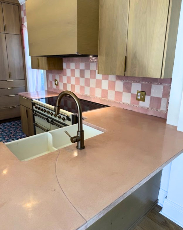 Modern kitchen with tan countertops, white undermount sink, black faucet, stainless steel range, and pink checkered backsplash tile
