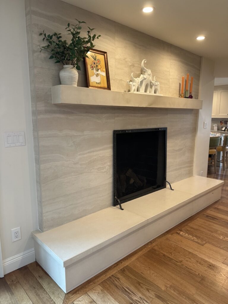 Modern fireplace with cream tile surround, white mantel shelf decorated with vase, framed art, white elephant figurines and candles, positioned above white hearth in home interior