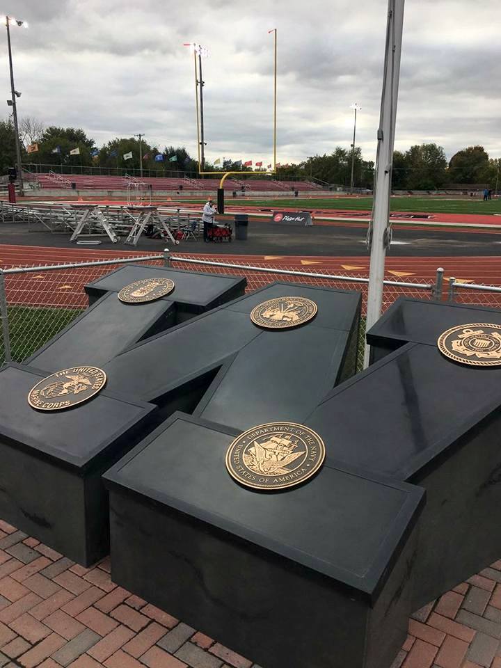 Black W shape with gold seals at a sports stadium memorial, with red track and field visible in background