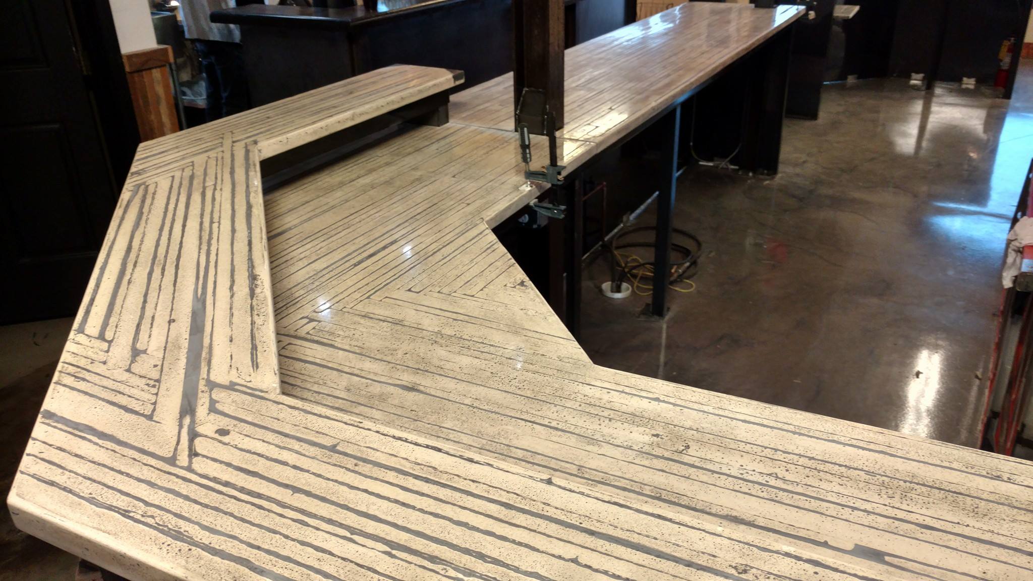 Light wood bar counter with linear grain pattern in a Cincinnati warehouse space, with black support bases and concrete flooring