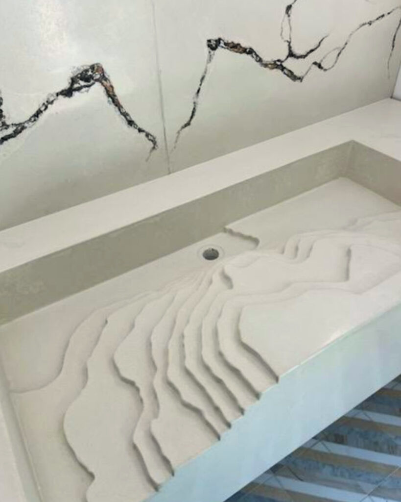 White bathroom sink with rippled texture design and visible crack patterns on wall above, showing structural damage