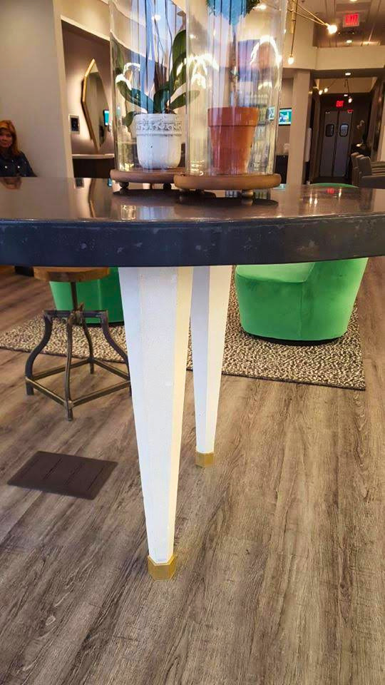 Modern desk with curved black countertop, white cylindrical supports with gold accents, and green upholstered seating in contemporary lobby