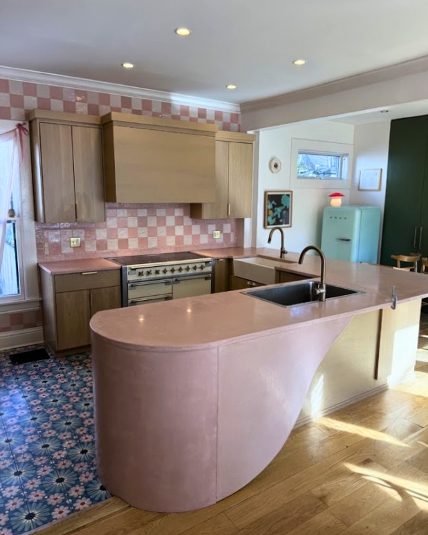 Modern kitchen with pink curved island, checkered backsplash, wooden cabinets, stainless steel range, retro mint refrigerator, and patterned blue floor
