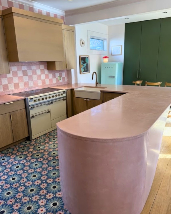 Retro-style kitchen with pink island, cream cabinetry, pink checkered backsplash, vintage stove, mint green refrigerator, and colorful patterned floor tiles