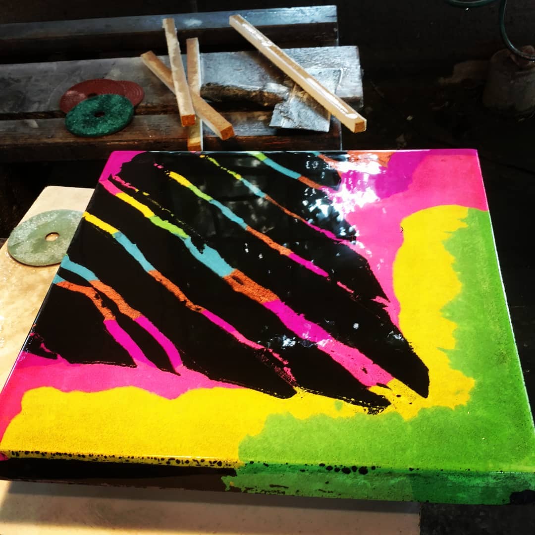 Vibrant pop art style canvas with neon pink, yellow, green, and black paint featuring diagonal colorful streaks, displayed in a Cincinnati workshop with painting supplies and wooden tools nearby