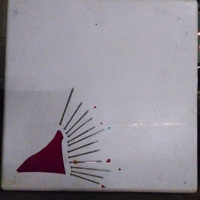 Handcrafted geometric art featuring a burgundy triangle with radiating gray lines and small colored accents on white paper
